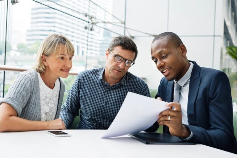 a picture of a couple looking at a paper their financial advisor is showing them and they all look surprised in a bad way